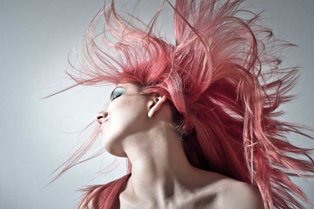 What Makeup is Vegan? This image catches an action shot of a woman with hair pink hair. As she flips her head to the side, the hair is wild with movement. Her makeup is done with prominent eyebrows and strong blue eyeshadow.