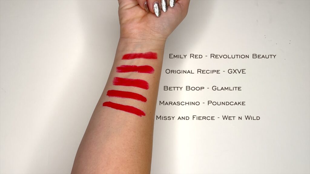 The underside of a forearm is swatched with 5 different red lipsticks. Each one is labeled. Annmarie Gustafson of Unfiltered Makeup shares the Best Red Lipsticks.